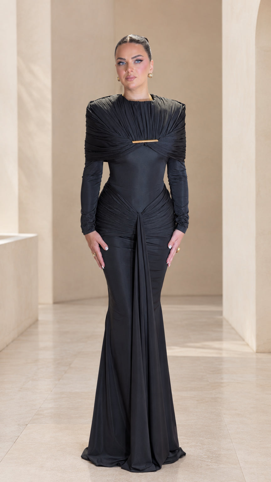 Front full view of black pleated cape long sleeve maxi evening gown with gold bar accent