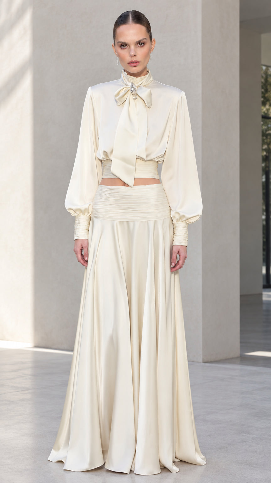 Front view of model wearing ivory satin bow tie blouse and matching pleated maxi skirt set