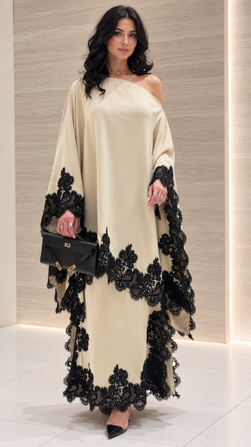 Front view of woman wearing cream one-shoulder draped maxi dress with black lace trim