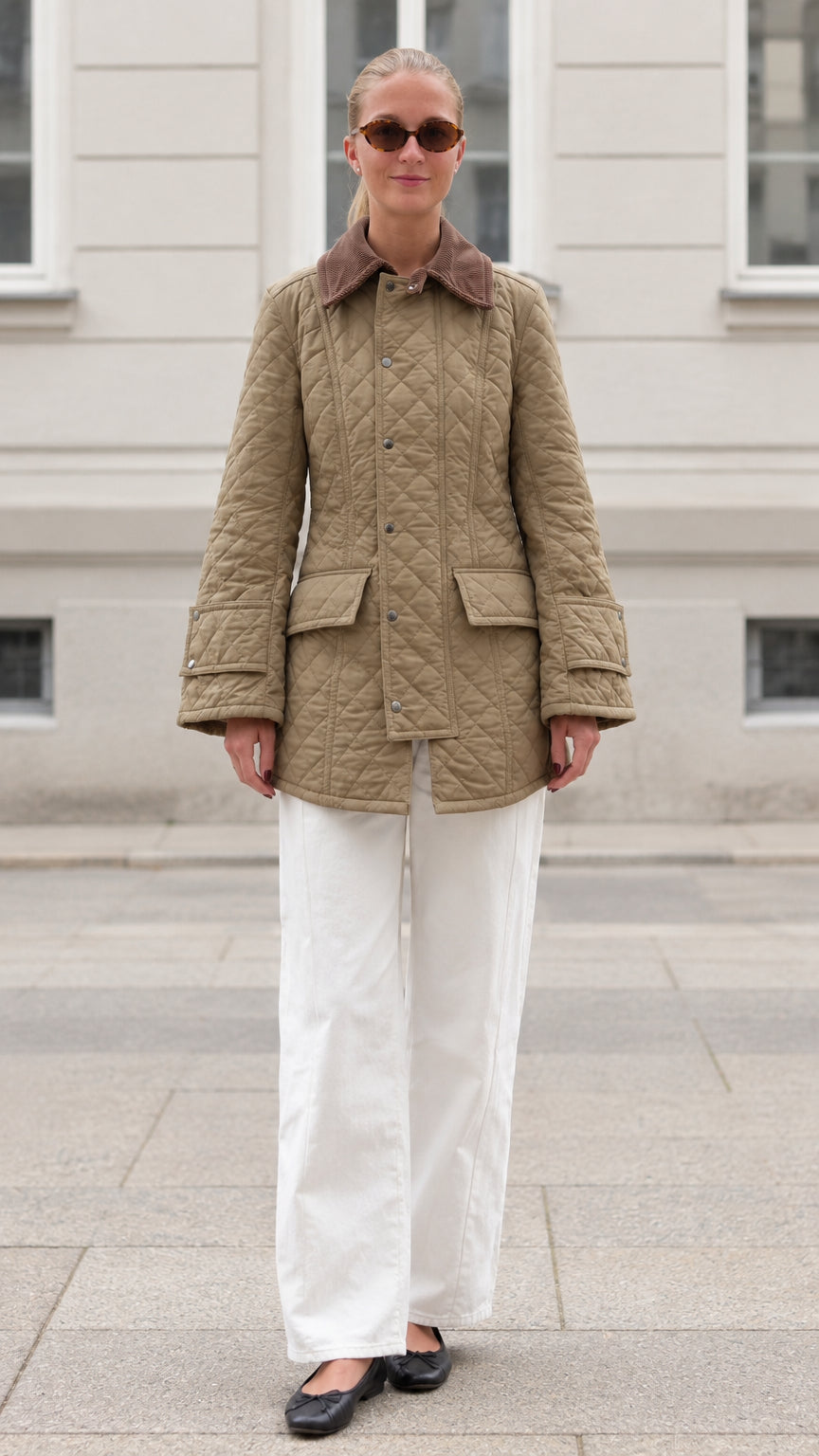 Front full-length view of woman wearing khaki diamond quilted barn jacket with white pants