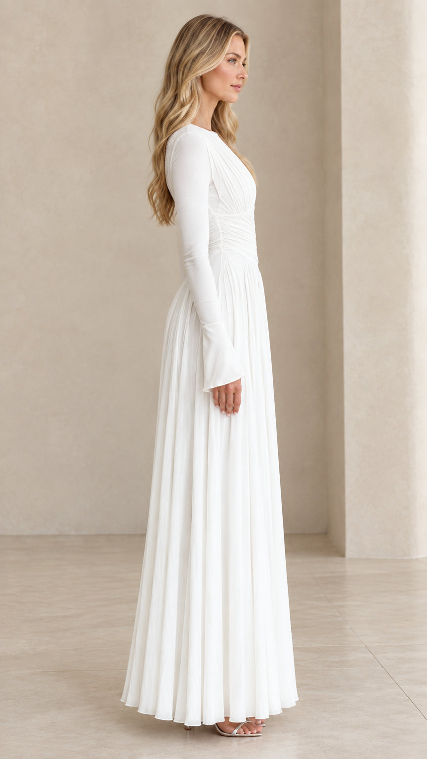 Side profile view of model in white pleated long sleeve formal gown