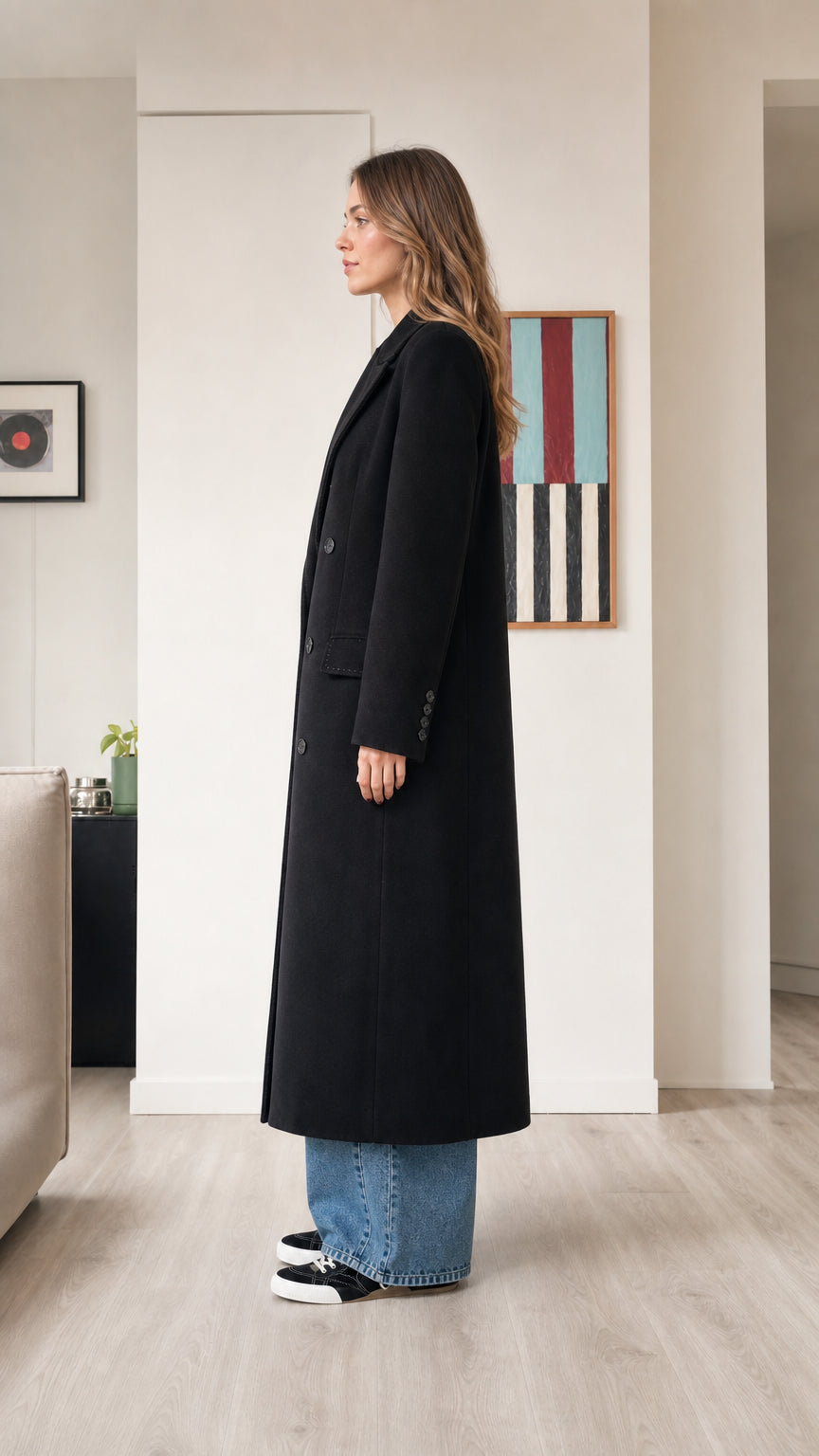 Side profile view of woman wearing black longline overcoat with wide-leg jeans