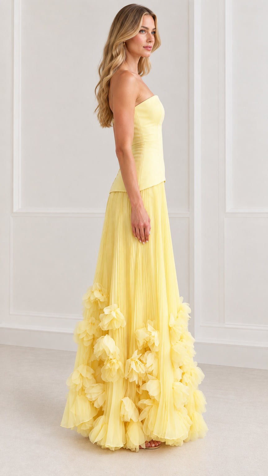 Side profile of model in yellow pleated strapless evening gown with floral details