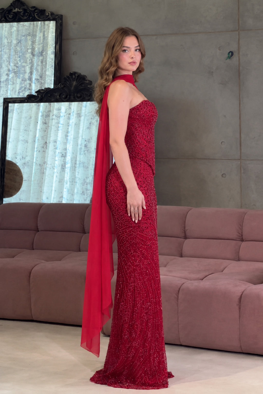 Side profile of the red sequin strapless formal gown showing floor-length fit and cape drape