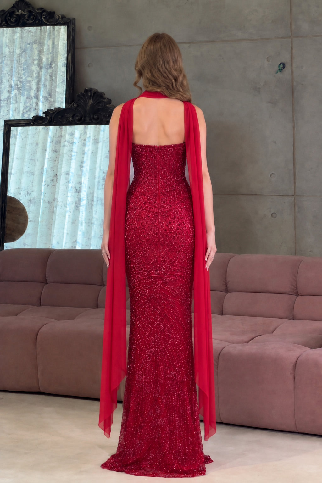 Back view of the red embellished evening dress showing low back design and long sheer scarf cape