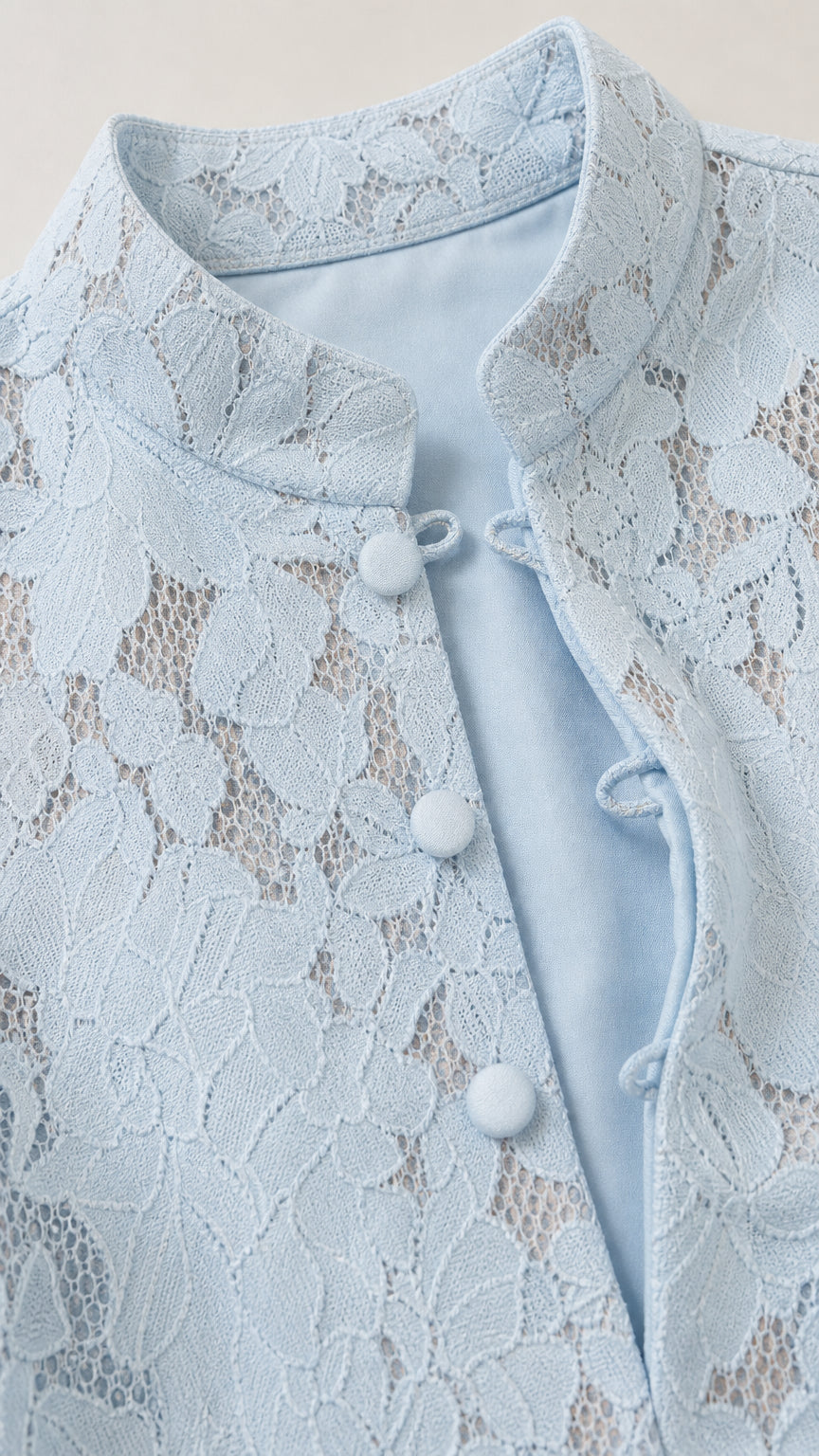Close-up detail of light blue floral lace, stand collar, and fabric-covered loop buttons