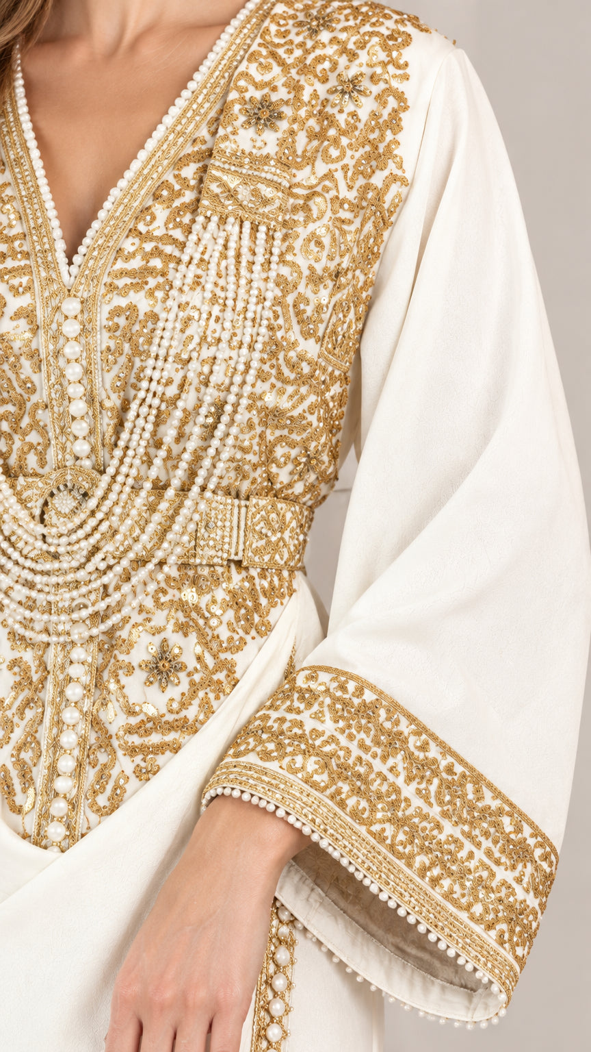 Close-up detail of ornate gold-tone embroidery and bead-like accents on white bodice