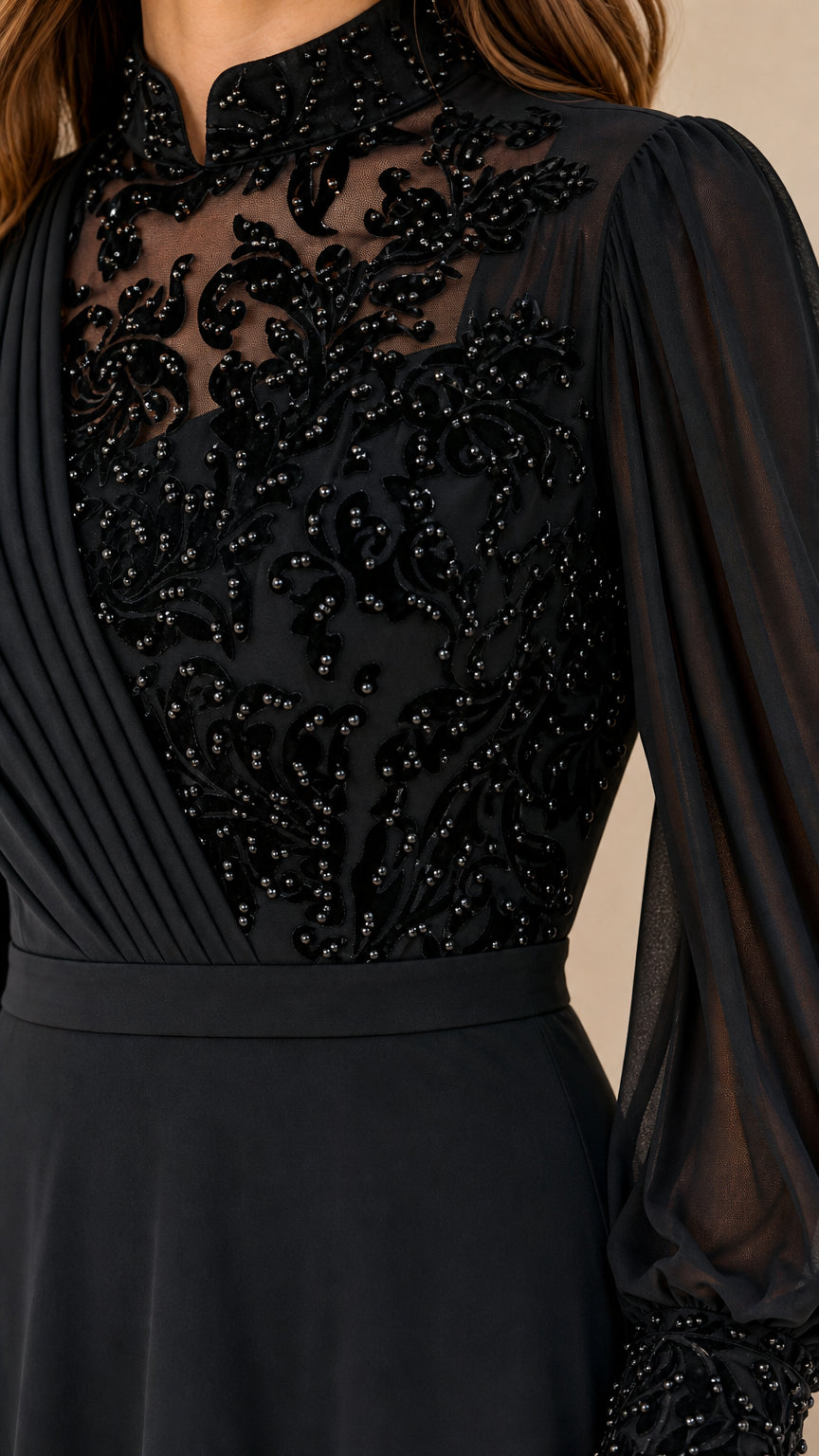 Close-up detail of beaded sheer neckline and pleated bodice on black evening gown