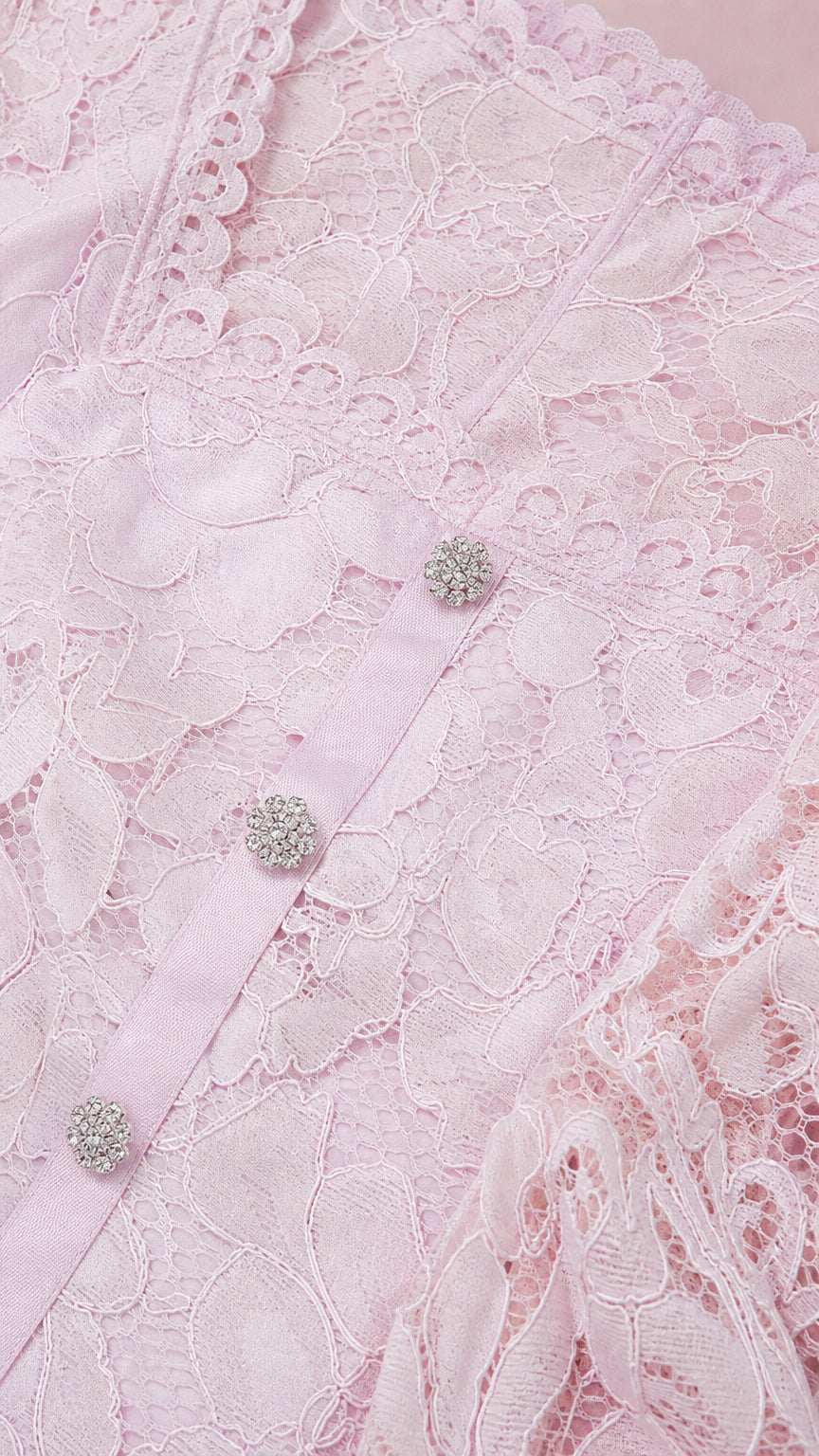 Close-up detail of the blush pink floral lace fabric, scalloped neckline, and crystal buttons