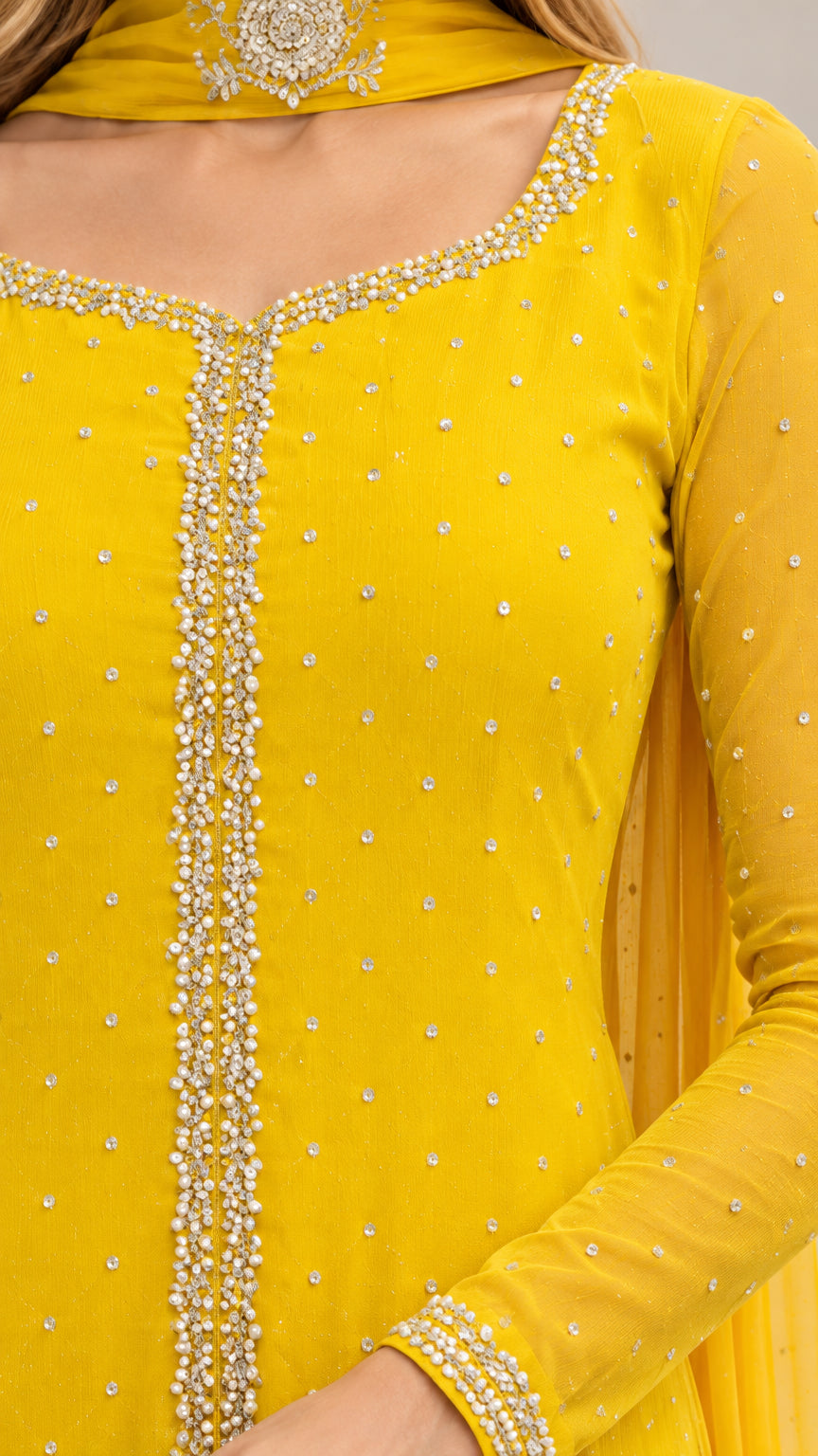 Close-up detail of yellow gown's beaded scoop neckline, sparkling accents, and sleeve cuff