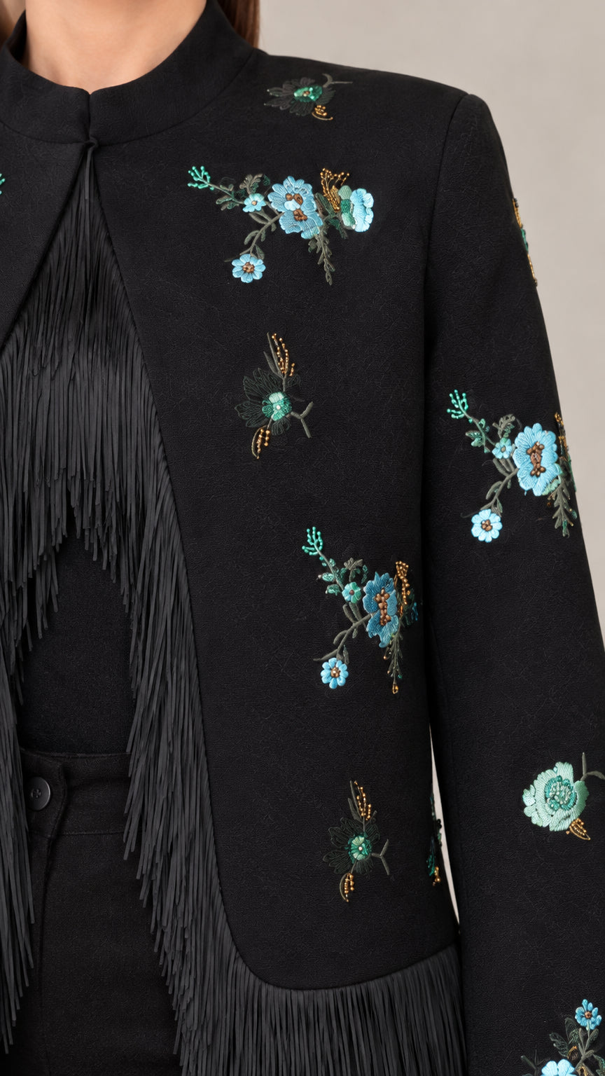 Close-up detail of turquoise floral embroidery and delicate black fringe on jacket