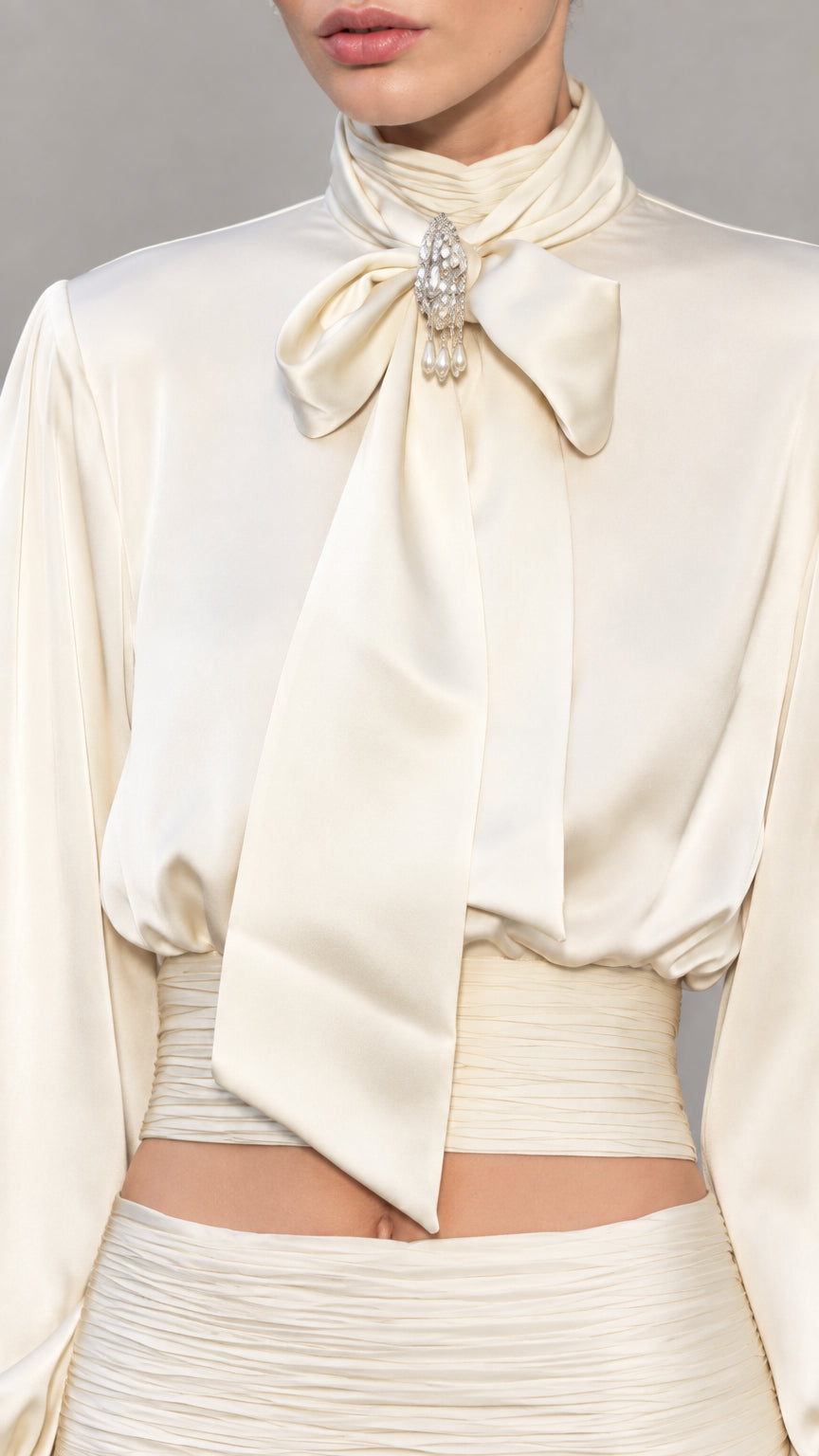 Close-up detail of high collar, bow tie, crystal brooch, and ruched waist on ivory satin top