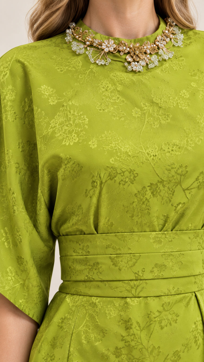 Close-up detail of jeweled neckline and floral jacquard texture on green dress