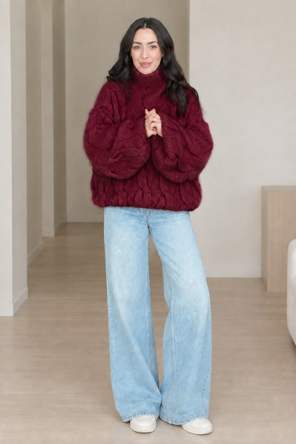 Front view of model wearing burgundy chunky cable knit turtleneck sweater with wide-leg jeans